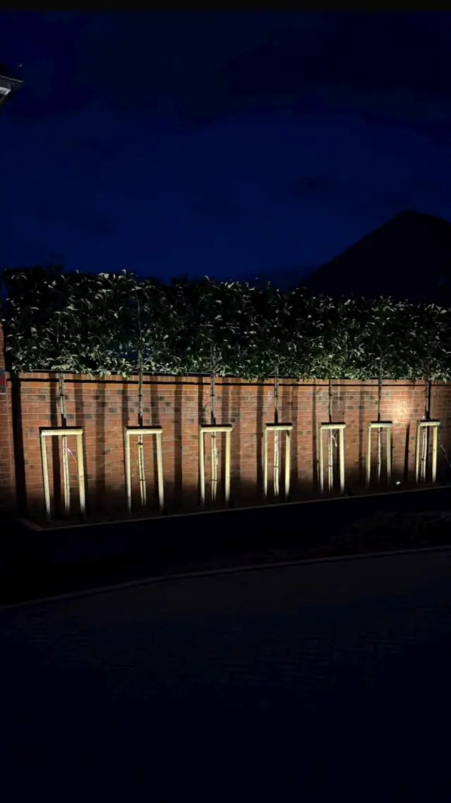 The same privacy wall lit up with warm uplights at night